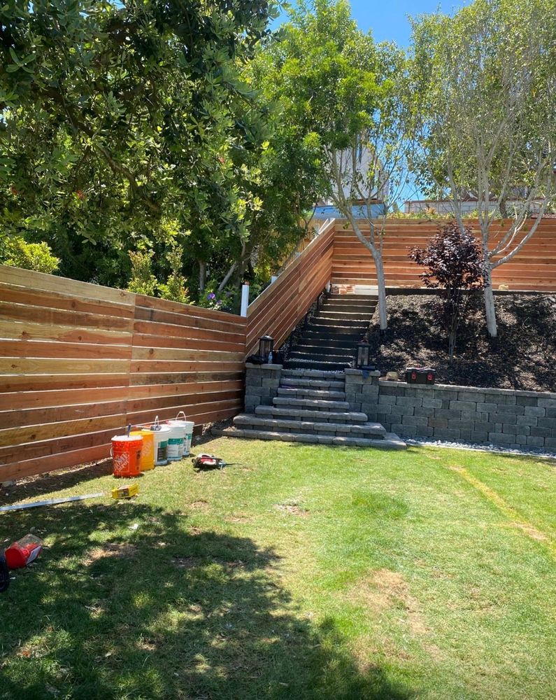 Hillside yard with cedar fence and block retaining wall stairs under construction